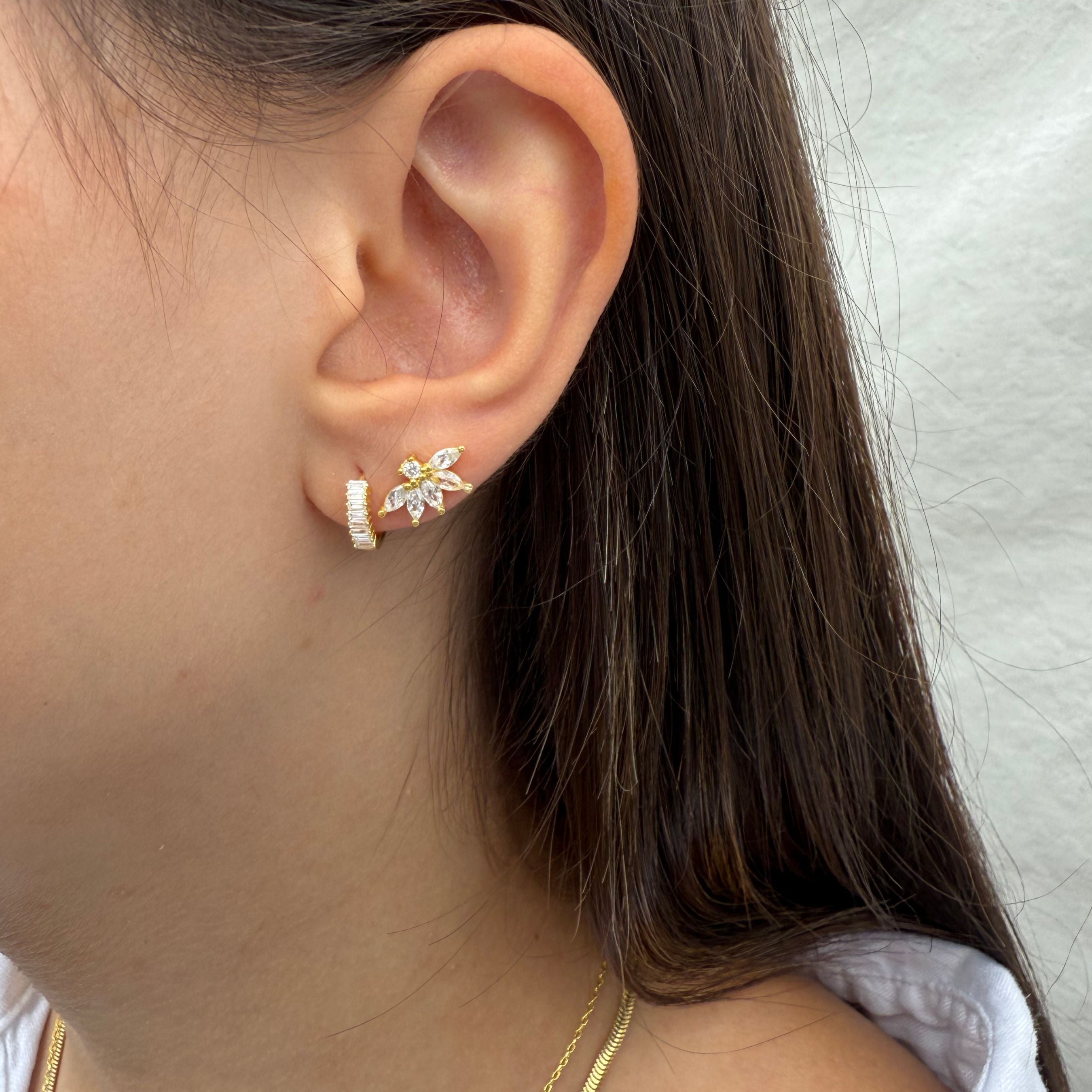 Close-up van gouden insteekoorbel met bladvormige zirconia, gedragen in het oor