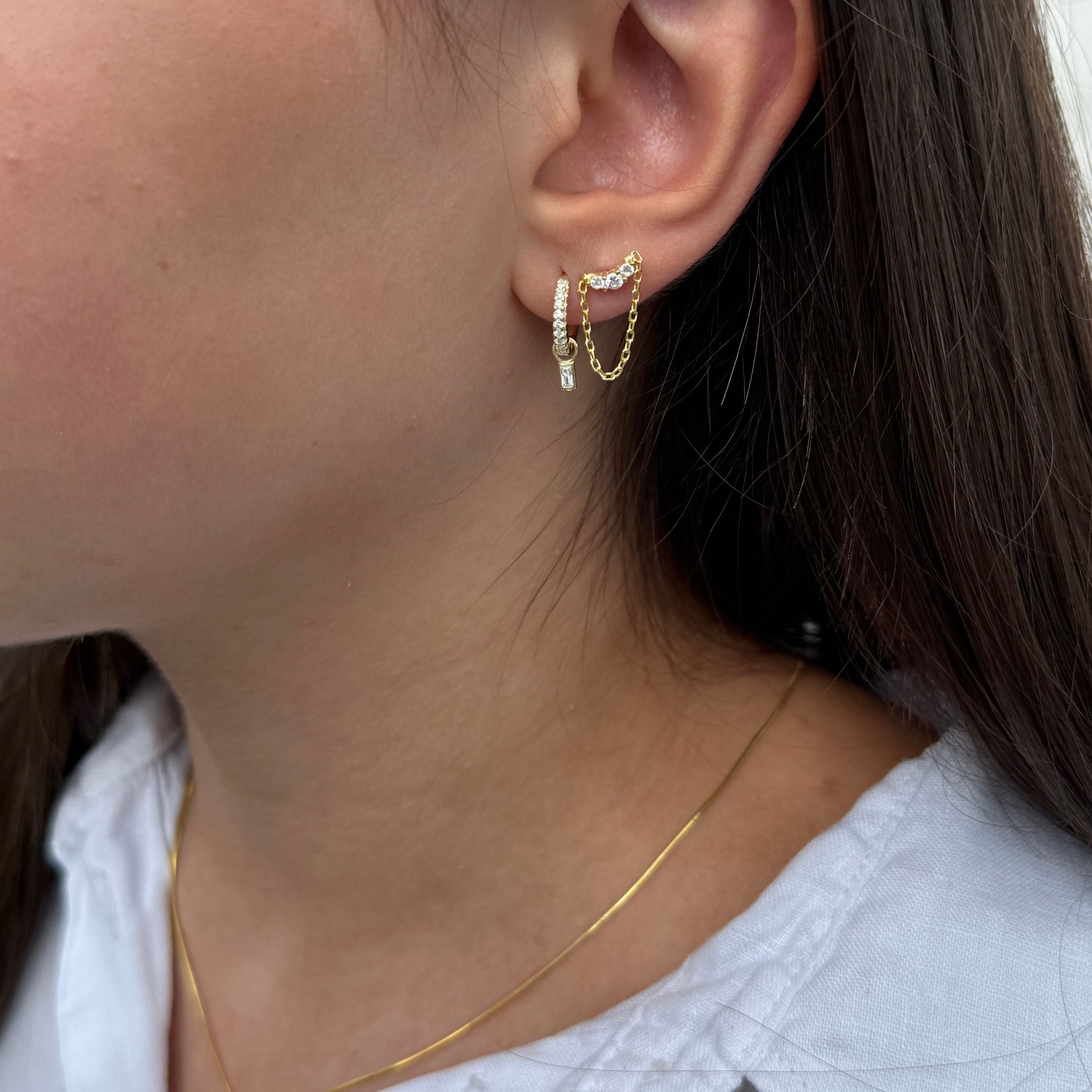 Close-up van gouden oorbel met dubbel kettinkje en zirkonia steentjes, gedragen in het oor