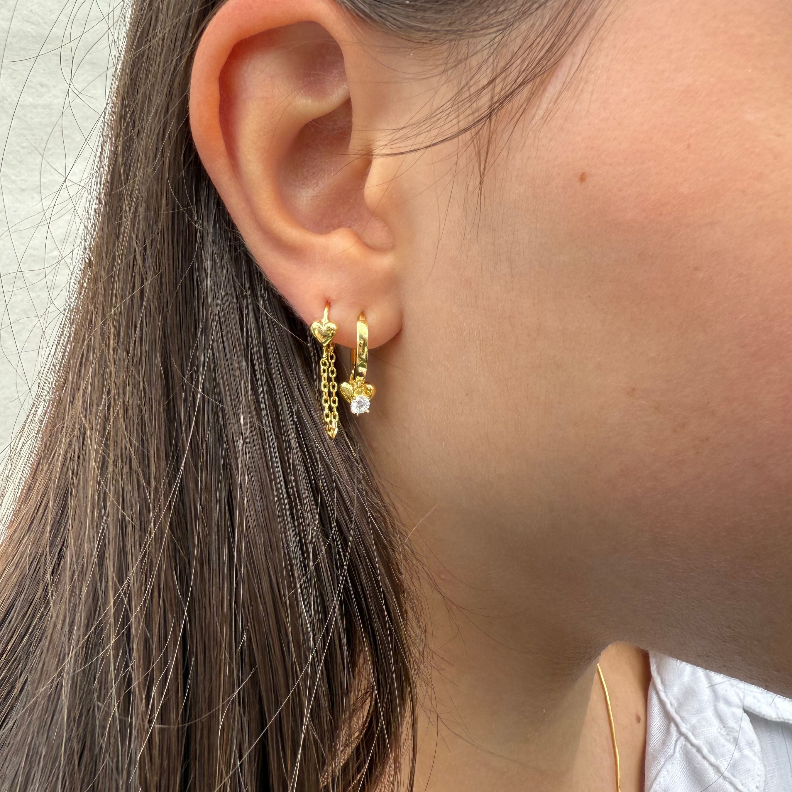 Close-up van gouden oorbel met hartjehanger en dubbele ketting, gedragen in het oor