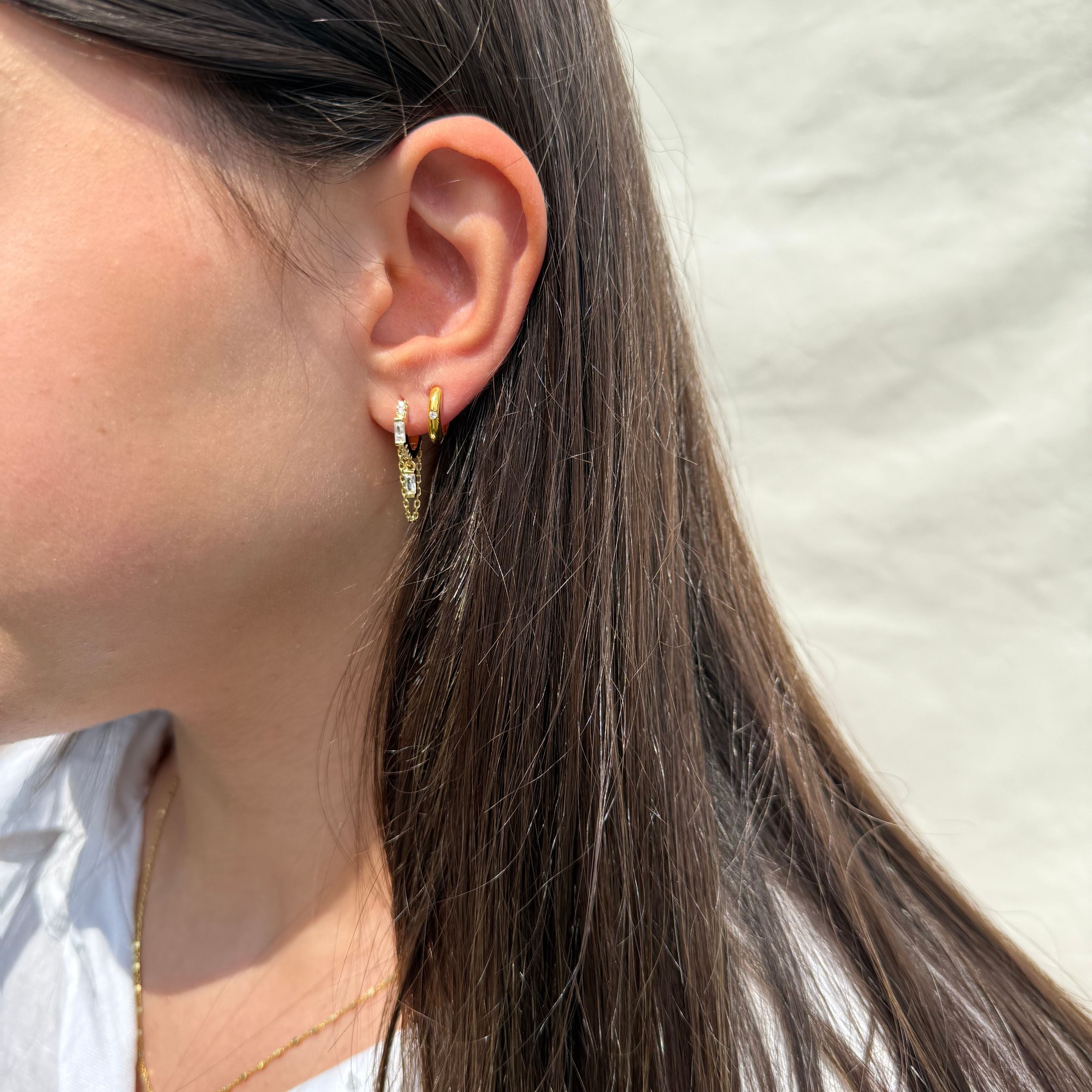 Close-up van een gouden oorbel met kettinkje en zirkonia steentjes, gedragen in het oor