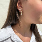 Close-up van gouden oorbel met bloemvormige zirkonia hanger en fijn kettinkje, gedragen in het oor